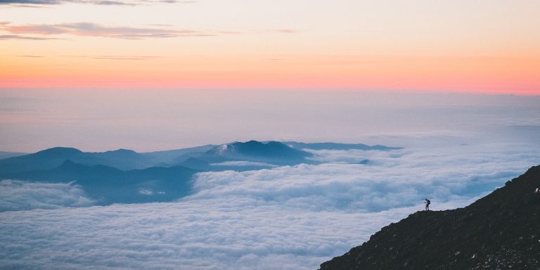 Foto von Rahil Chadha a person standing on a cliff above the clouds