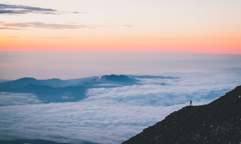 Foto von Rahil Chadha a person standing on a cliff above the clouds